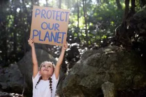 Kind hät Schild mit Aufschrift protect the planet hoch und fordert damit zu mehr Nachhaltigkeit auf