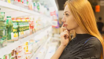 Eine junge Frau denkt über die Auswahl eines Joghurts im Kühlregal nach. Solche Situationen werden im Rahmen der Produktforschung beobachtet.